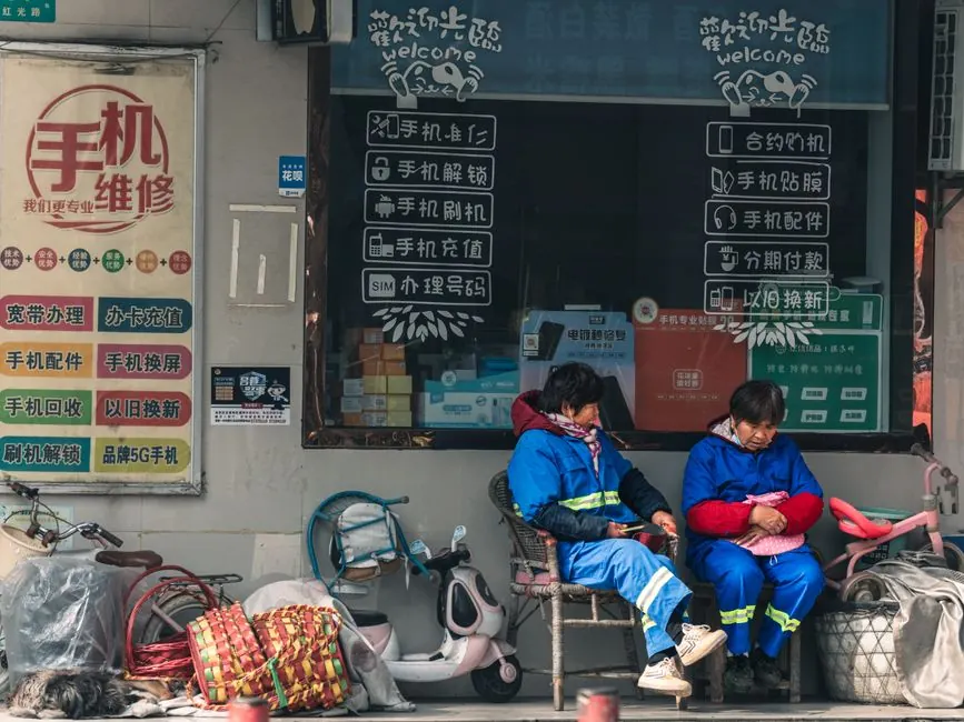 Two workers in blue uniforms rest outside a mobile repair shop with signage.